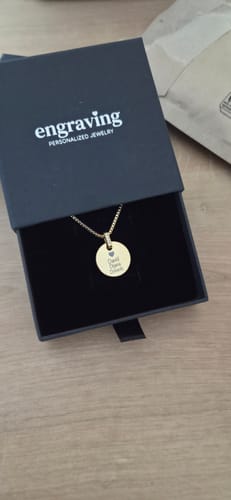 Customer's gold Stellar Names necklace with an engraved pendant, shown inside its black jewelry box.