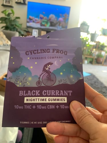 Reviewer holding the purple packet of Black Currant Nighttime Gummies in their living room.