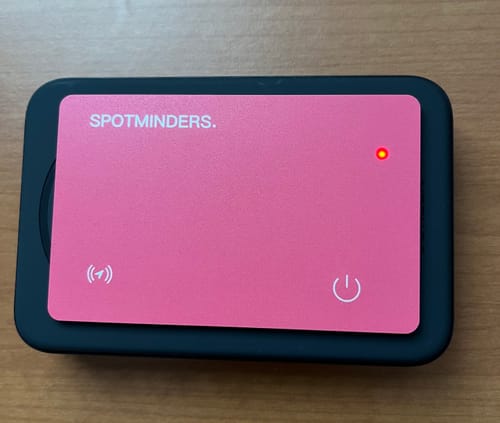 Customer's pink SPOTMINDERS Tracking Card charging on a black wireless charger, with its red indicator light on.