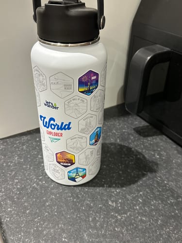 Customer's white World Explorer Bottle on a counter with several colorful destination stickers applied.