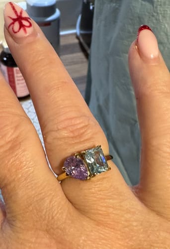 Customer's hand wearing the Toi Et Moi Birthstone Ring, with a purple pear-cut stone and a light blue emerald-cut stone.
