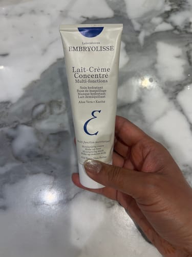 Reviewer holding the white tube of Lait-Creme Concentre against a marble background.