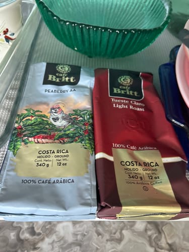 Customer displays two bags of Cafe Britt coffee: a Peaberry AA and a Tueste Claro Light Roast.