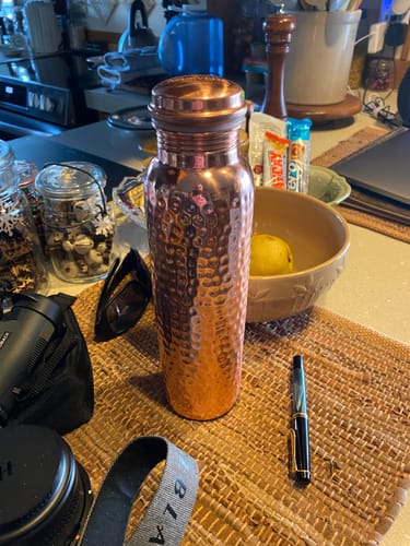 Customer's hand-hammered Pure Copper Water Bottle sitting on a woven placemat on a kitchen counter.