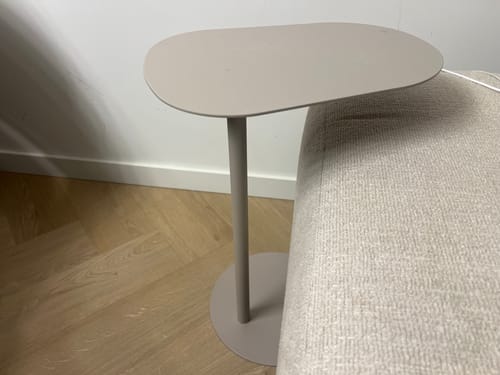 Klant toont de beige, organisch gevormde MISOU bijzettafel naast een bank.
