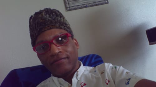 A reviewer wearing a patterned hat and red glasses looking at the camera.