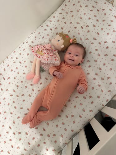 Customer's Personalized Strawberry Girl doll lying in a crib next to a smiling newborn baby.