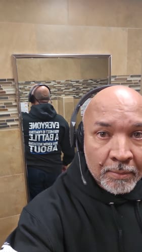 Reviewer takes a mirror selfie to show the message printed on the back of their black Be Kind hoodie.