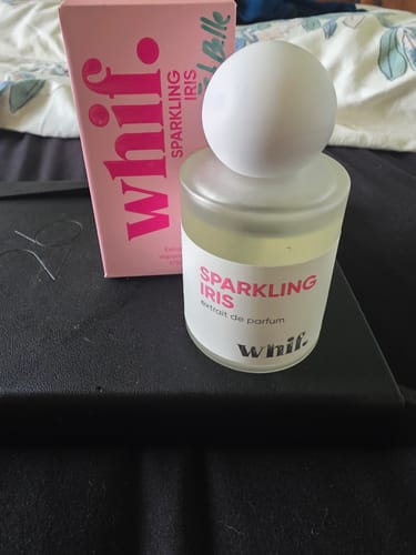 A customer's Sparkling Iris perfume bottle with its pink box resting on a black surface.