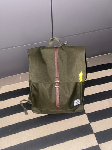 תמונת לקוח של תיק הגב City Mid בצבע ירוק זית מונח על שטיח פסים.