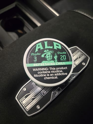 Reviewer's can of ALP Refreshing Chill Nicotine Pouches resting on a car's dark center console.