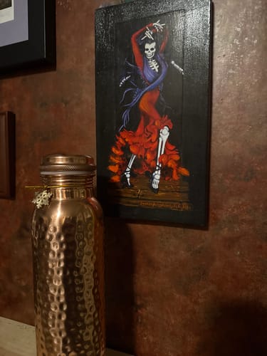 Customer's hand-hammered Pure Copper Water Bottle displayed on a shelf next to a painting.
