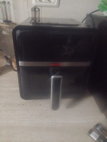 Recenzentul arată friteuza neagră cu aer cald în care se folosește tava de protecție din silicon.