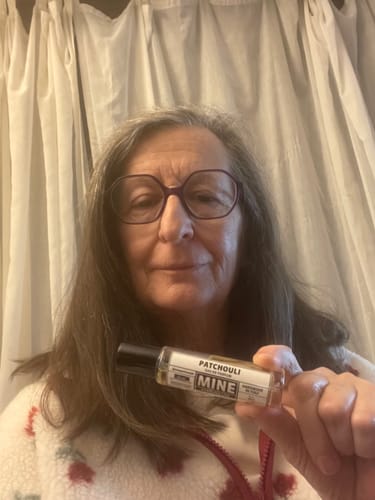 Recensore che mostra la piccola e trasparente boccetta di profumo Patchouli.