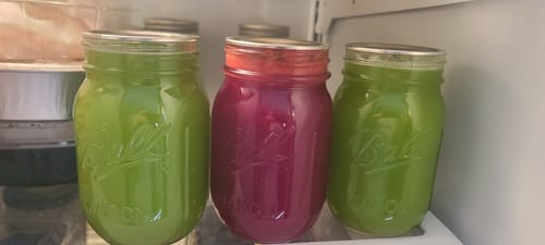 Customer's colorful juices in three mason jars, vacuum-sealed with the Mason Genie kit inside a refrigerator.