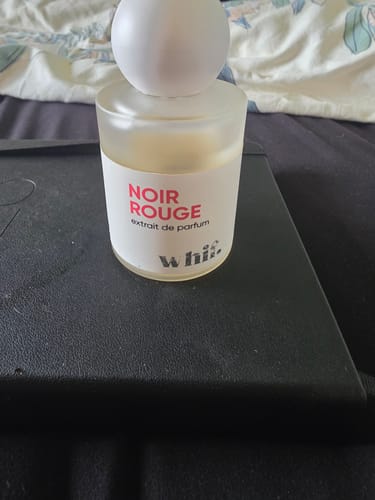 Customer's bottle of Noir Rouge perfume, showing the frosted glass bottle and white round cap on a dark surface.