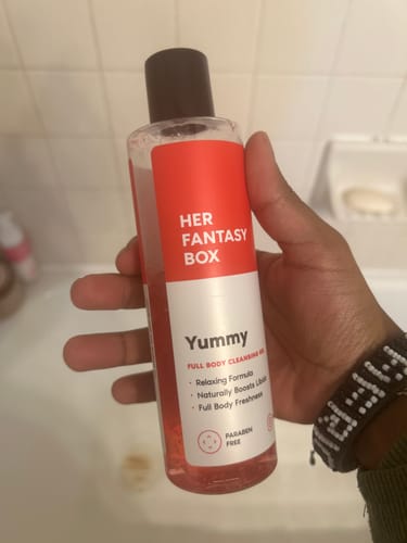 Customer holds the clear bottle of pink Yummy Organic Body Wash in their bathroom.