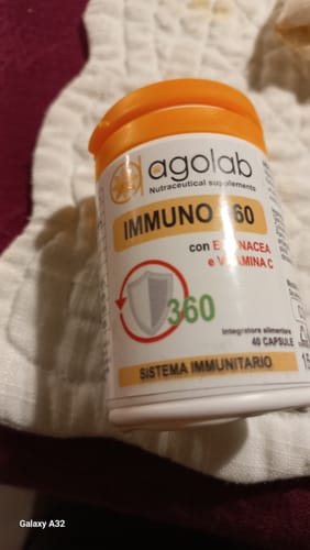 Recensore mostra la confezione bianca di Immuno 360 con tappo arancione, appoggiata su un tessuto.