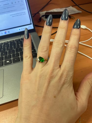 Customer's hand wearing the Leesha Birthstone Ring, showing the green and clear pear-shaped stones on a gold band.