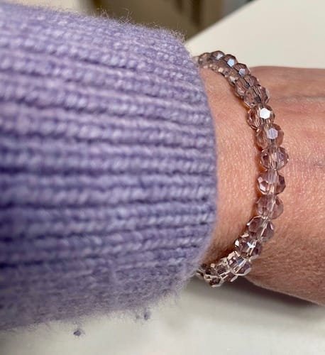 A customer's wrist wearing the faceted Amethyst Crystal Stacker bracelet next to a light purple sweater sleeve.