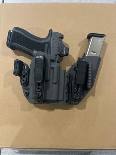 Customer's custom dark gray holster holding a pistol and a spare magazine, seen from above on a cardboard surface.