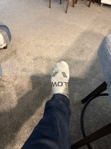 A customer's foot wearing a light gray Men's Alpaca Sock indoors.