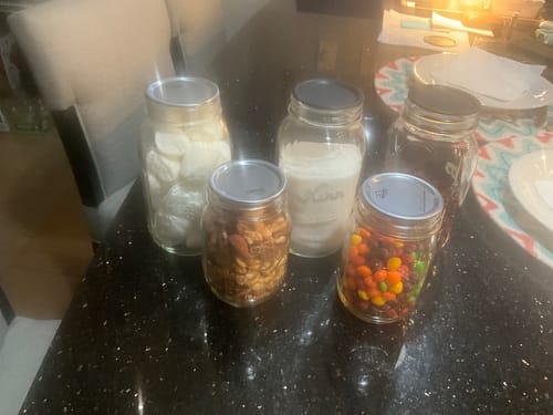 Customer's photo of five sealed glass jars filled with snacks like candy and nuts on a dark countertop.