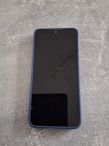 Rezensent zeigt die 3-in-1-Schutzfolie mit einem Riss auf einem Smartphone in einer blauen Hülle.