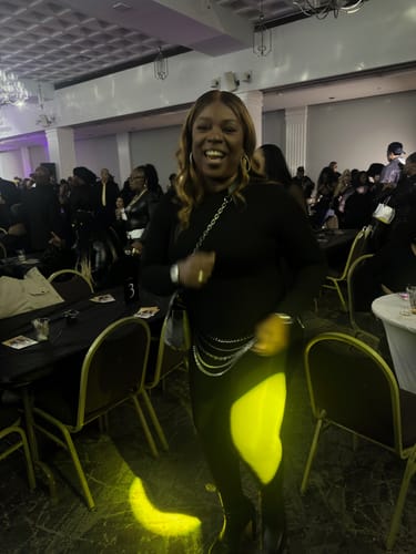 Reviewer smiling at an event while wearing the black NW Sculpt Jumpsuit, styled with a chain belt.