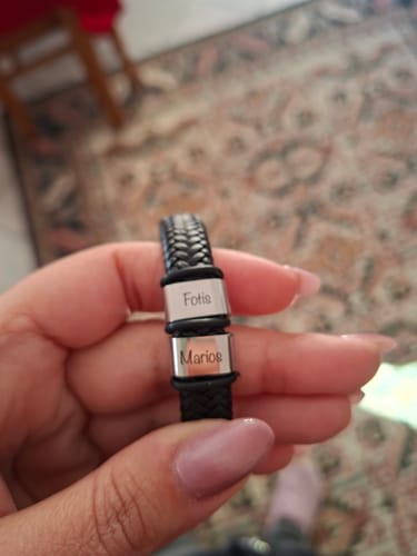 Customer's hand holding the black braided Viking bracelet with two steel beads engraved with the names 'Fotis' and 'Marios'.