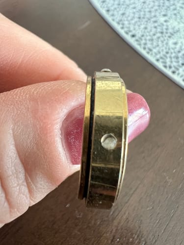 Customer holding the gold Spins Love Ring, showing a close-up of an empty setting where a stone is missing.