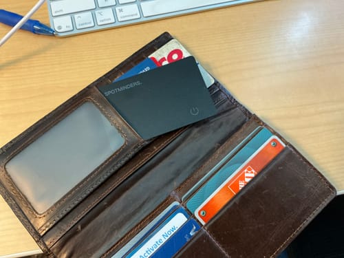 Customer's black SPOTMINDERS Tracking Card placed inside an open brown leather wallet on a desk.
