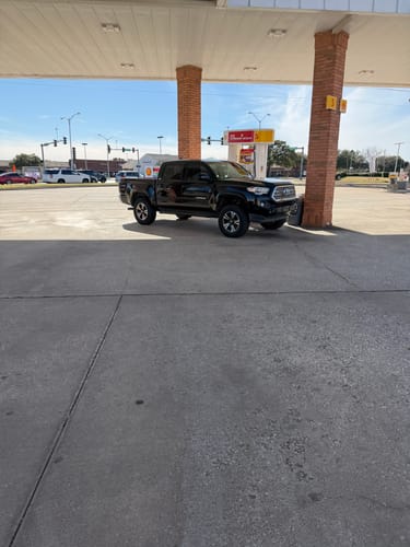 Customer's black Toyota Tacoma at a gas station, showing the raised, level stance from the 3" front leveling lift kit.