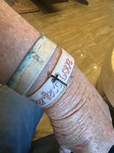 Customer wearing a fabric bracelet on their wrist, accessorized with the small silver Cross Bracelet Charm.