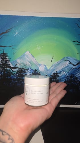 Customer holding the white jar of Raspberry Hand Cream in their open palm.