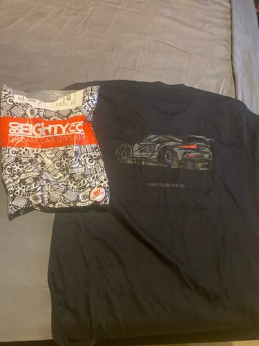Customer's black DCG85 shirt with a cool car graphic laid out on a bed next to its packaging.