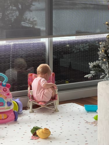 A customer's baby sitting in the pink patterned Amy baby chair v2, seen from behind in a playroom.