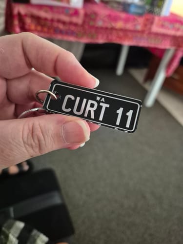 Reviewer holding a custom black license plate keychain that reads 'CURT 11'.