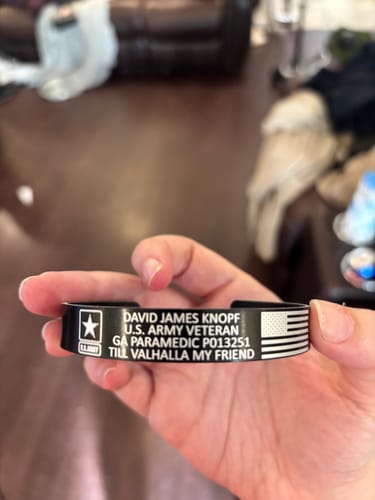 Customer holding their custom black bracelet engraved with text, a U.S. Army logo, and an American flag.