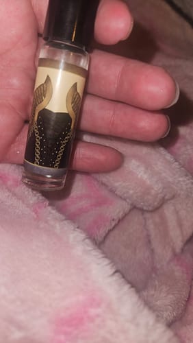 Close-up of a reviewer holding a small roll-on bottle of Cersei perfume in their hand against a pink blanket.