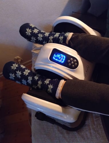 Anmelder slapper af med fødderne i det hvide fod- og lægmassageapparat, mens de har mønstrede sokker på.