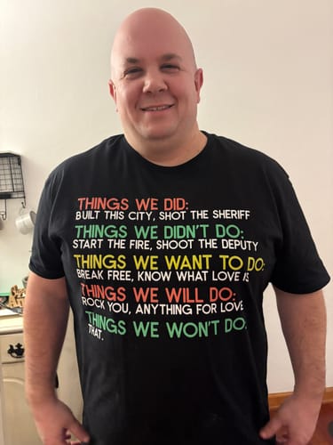 Customer smiling while wearing the black Things We Did T-Shirt with colorful text.