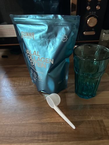 A customer's blue pouch of Halal Collagen Protein sits on a kitchen counter next to a scoop and a glass.