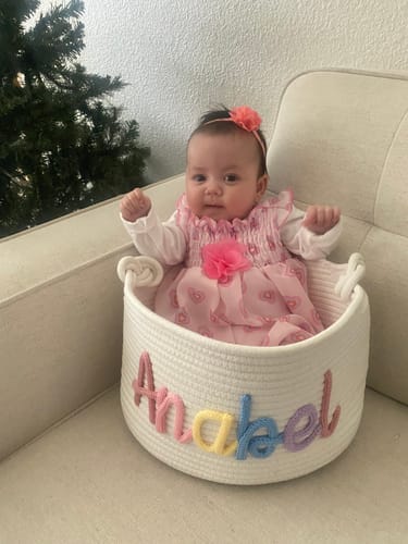 Reviewer's personalized white basket with a baby sitting inside. The name 'Anabel' is stitched in colorful yarn on the front.