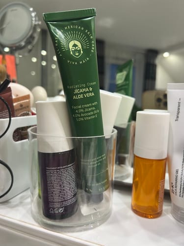 Reviewer's Radiating Cream tube standing in a clear glass holder with other skincare products on a vanity.