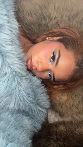 Close-up of a reviewer lying down, showing the texture of the plush, light blue Faux Fur Pelted Mini Skirt's matching top.