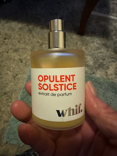 Customer holding the clear bottle of Opulent Solstice perfume with golden liquid against a carpeted background.