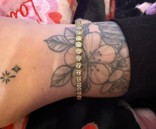 Customer wearing the gold-tone Classic Bezel Tennis Bracelet on their tattooed wrist.