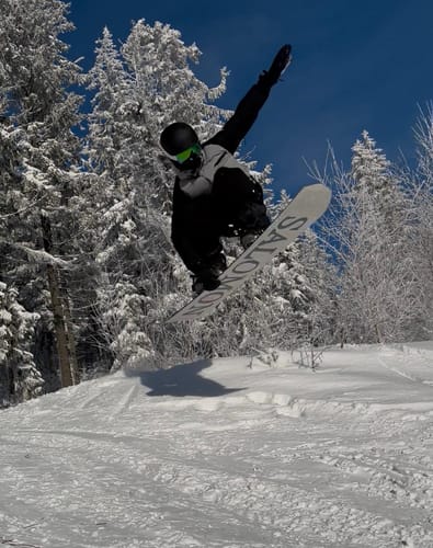 Reviewer in black Baggy Snow Pants jumping on a snowboard on a snowy mountain.