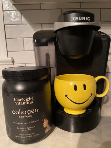 Reviewer's BGV Collagen Powder container on a kitchen counter next to a coffee maker and a yellow mug.